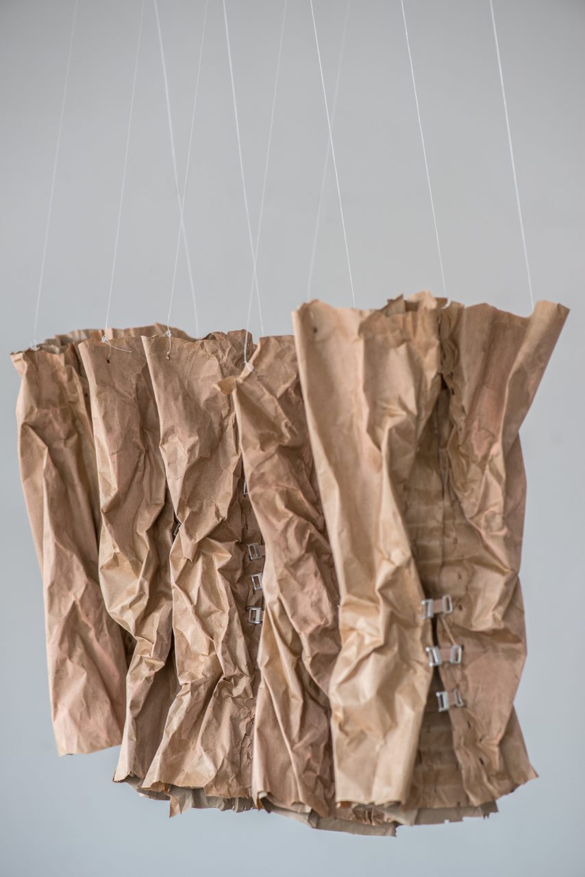 uniform 2013, make-up on paper, bandage clips, 100 x 170 cm. uniform describes the sometimes painful effort to achieve individuality, which can also become a corset, as well as the social group pressure of fashion and status that makes many look similar. The paperwork is very light and hangs on transparent fishing tendons from the ceiling. The group of paper corsets moves in step as it passes through the light draught of air.